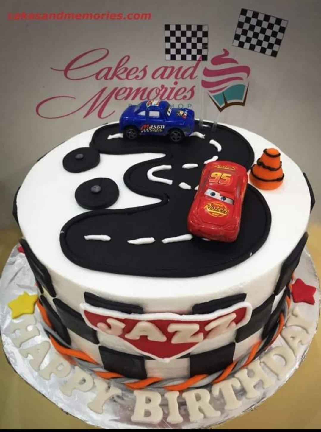 Disney Cars themed birthday cake with Lightning McQueen and Doc Hudson toy cars on a black fondant road with checkered flag toppers.