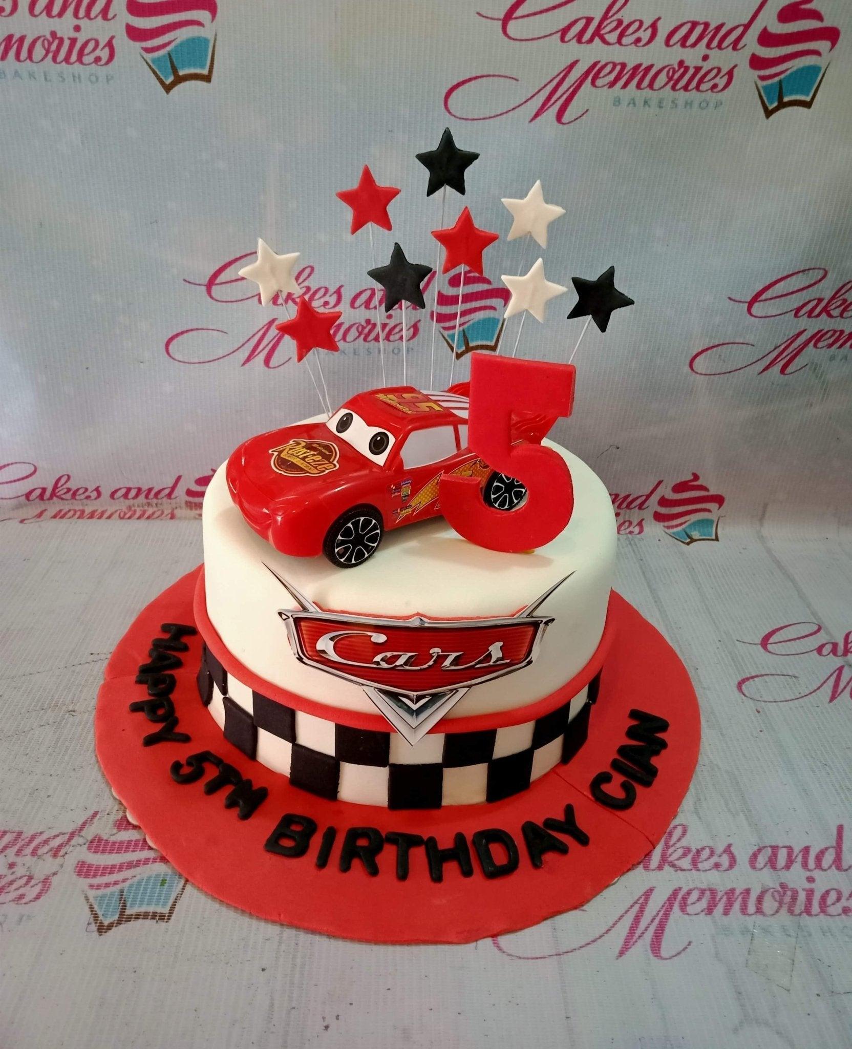 Disney Cars themed 1-tier fondant cake with Lightning McQueen toy topper and checkered racing flag pattern on a red base board.