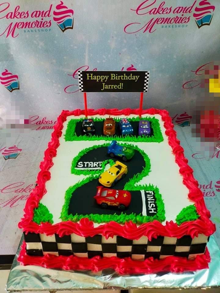 Disney Cars themed rectangle birthday cake with a number 2 racetrack design, toy cars, and red icing borders.