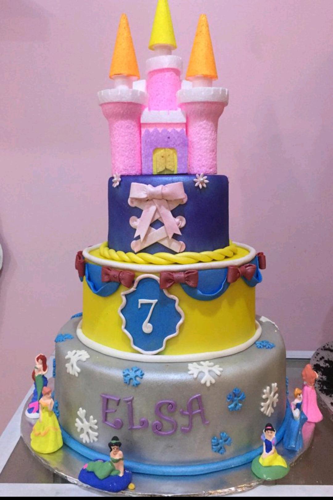 Three-tier Disney Princess themed fondant cake with a pink castle topper, princess figurines, and snowflake decorations.
