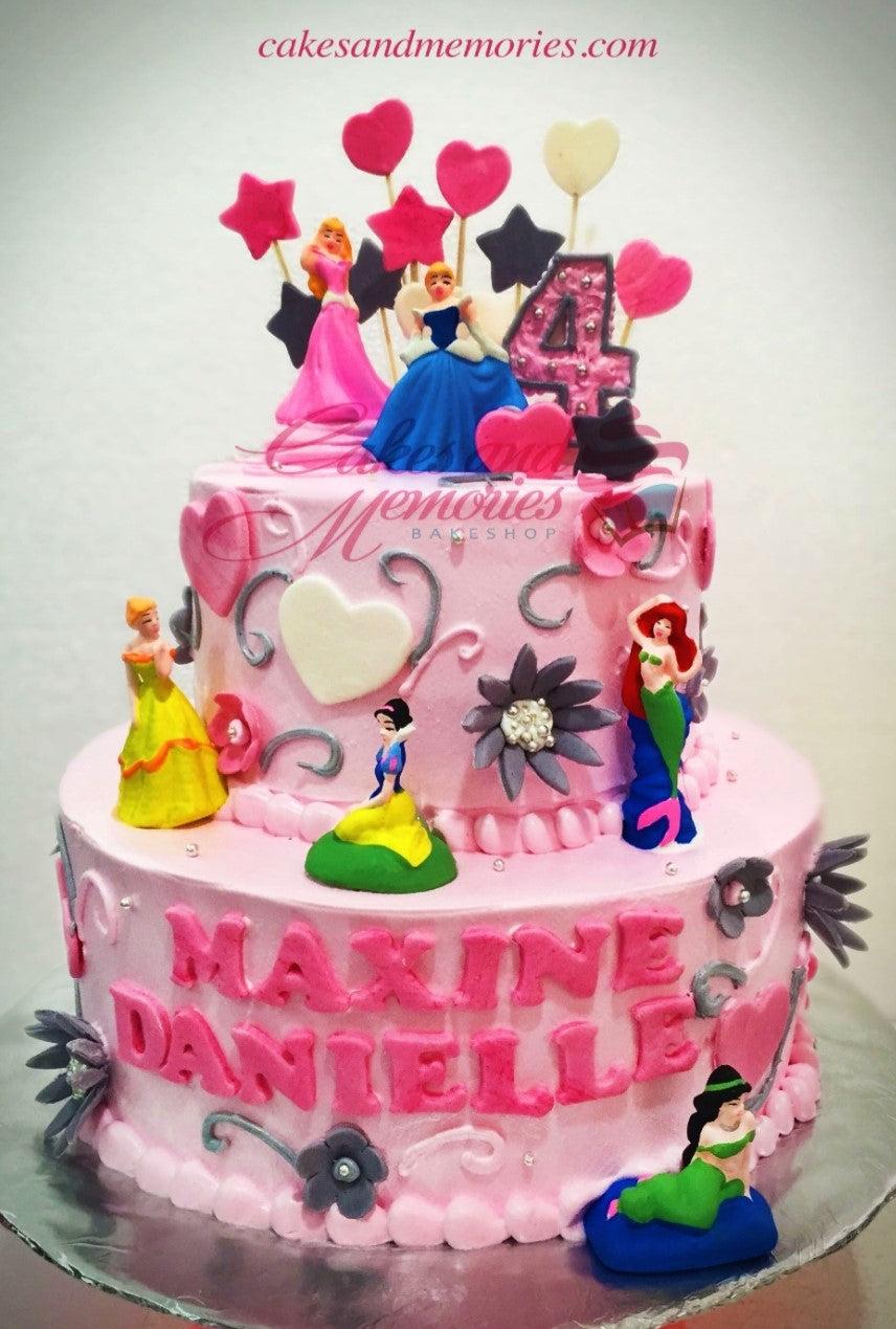 Pink 2-tier Disney Princess birthday cake with figurines of Aurora, Cinderella, Snow White, Ariel, Belle, and Jasmine.