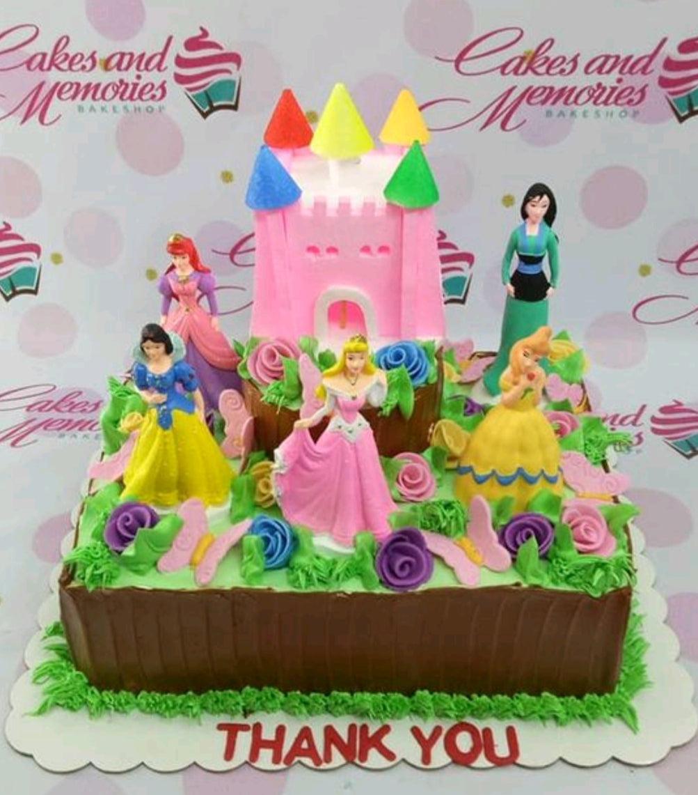 Disney Princess themed rectangle cake with a pink castle topper, figurines of Snow White, Aurora, Belle, Mulan, and Ariel, and colorful icing roses.