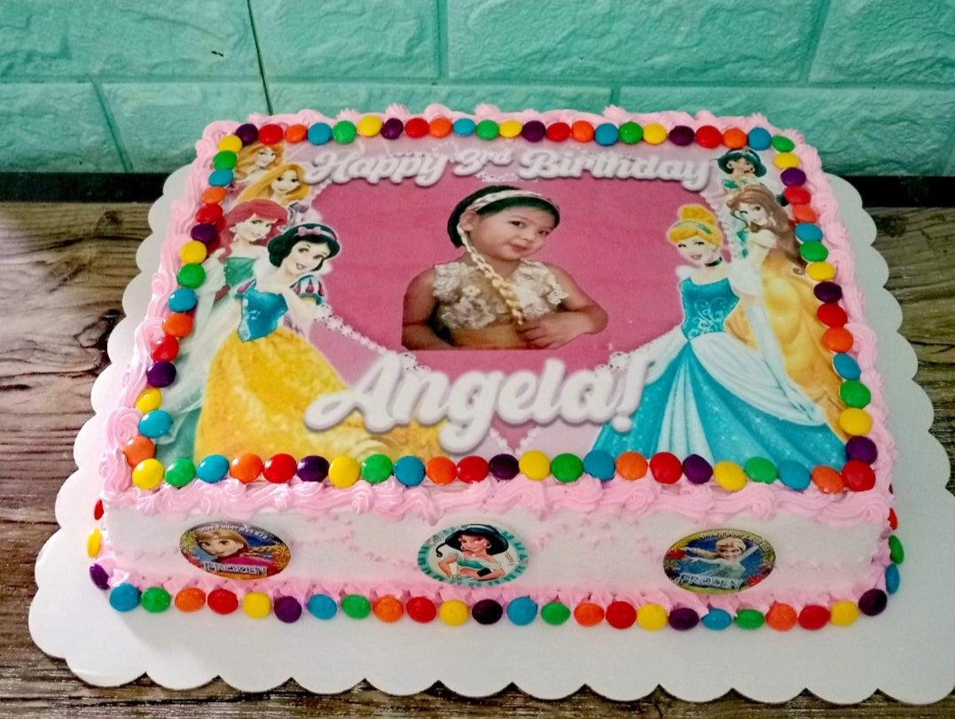 Pink rectangular Disney Princess birthday cake with a photo of a young girl and colorful candy borders.