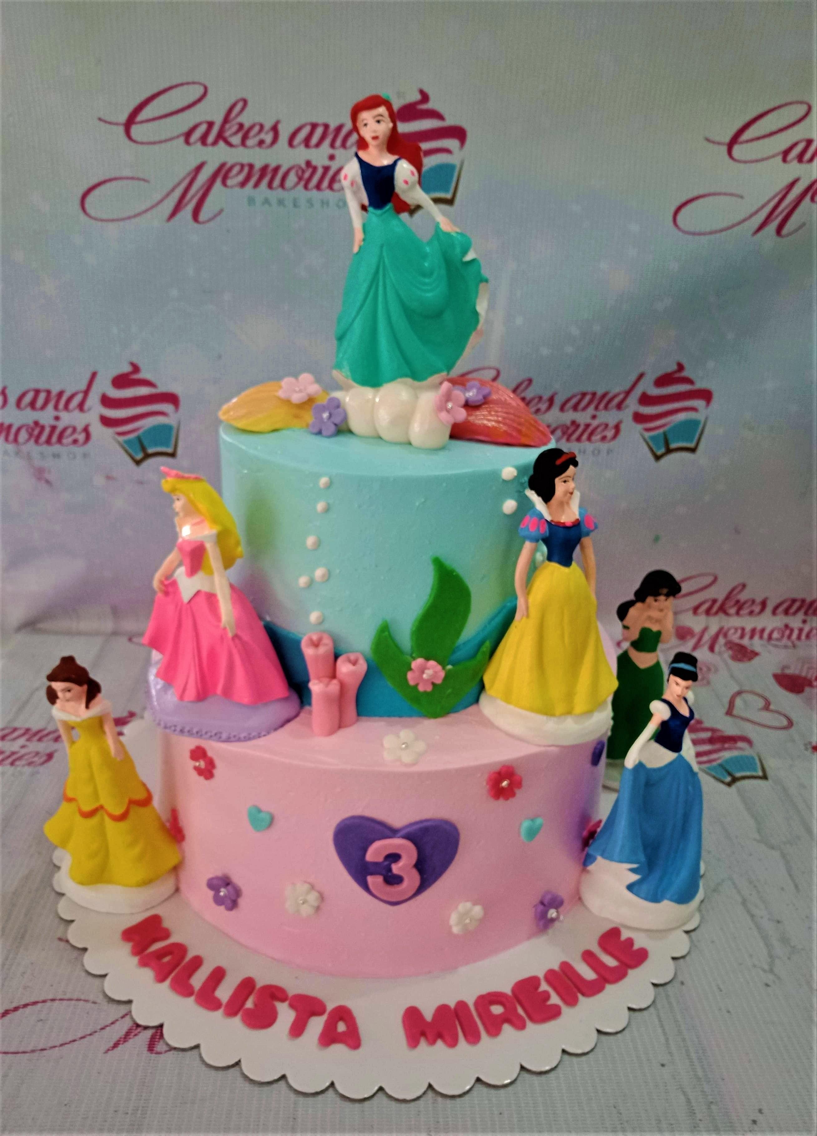 Two-tier Disney Princess themed cake in pink and light blue with Ariel, Belle, Aurora, Snow White, Jasmine, and Cinderella figurines.