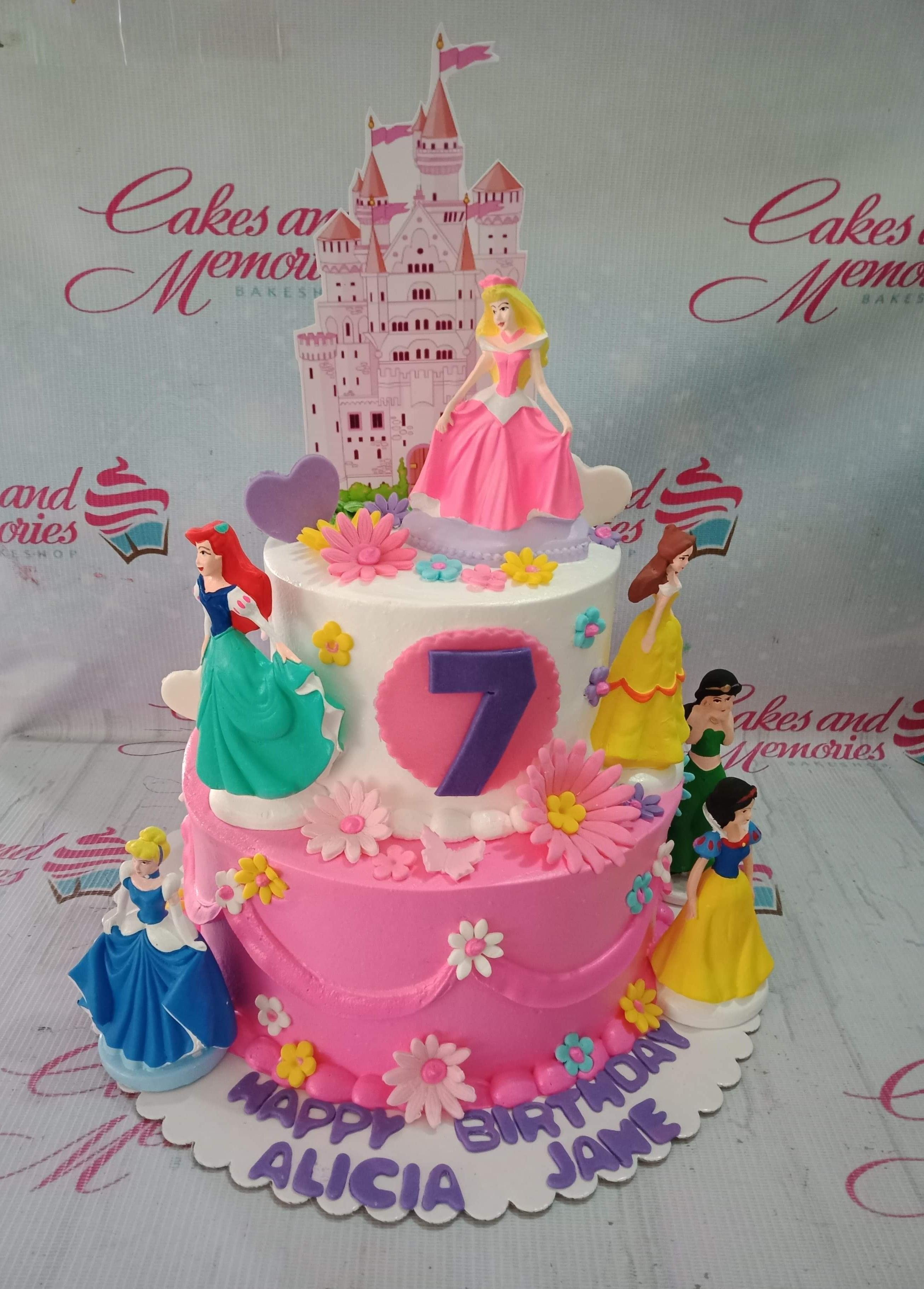 Two-tier pink and white Disney Princess themed birthday cake with figurines of Aurora, Ariel, Belle, Jasmine, Snow White, and Cinderella.
