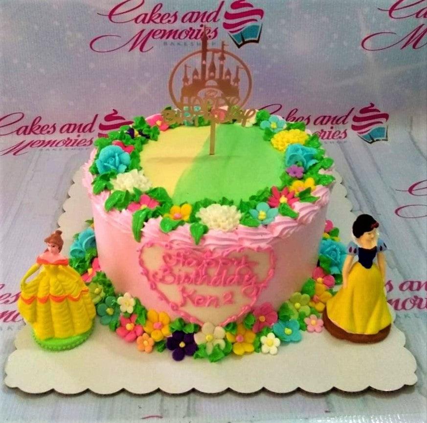 Pink princess birthday cake with Belle and Snow White figurines, a gold castle topper, and colorful icing flowers.