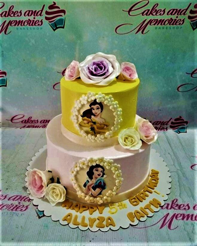 Two-tier Disney Princess cake with Belle and Snow White printouts, decorated with pink and white gumpaste roses on yellow and pink icing.