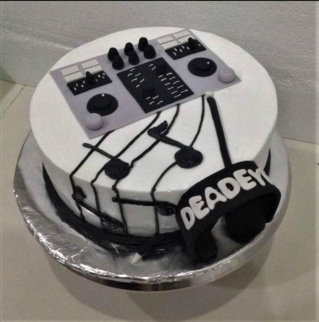 White round cake with a DJ controller topper, black music notes on the side, and a black headphone decoration with the name DEADEYE.