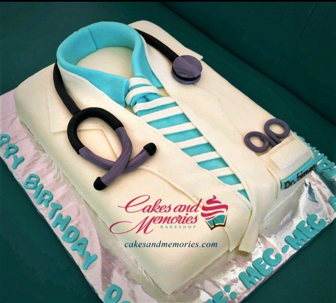 Doctor's coat rectangle fondant cake with a stethoscope, striped tie, and medical scissors decorations in white, teal, and purple.