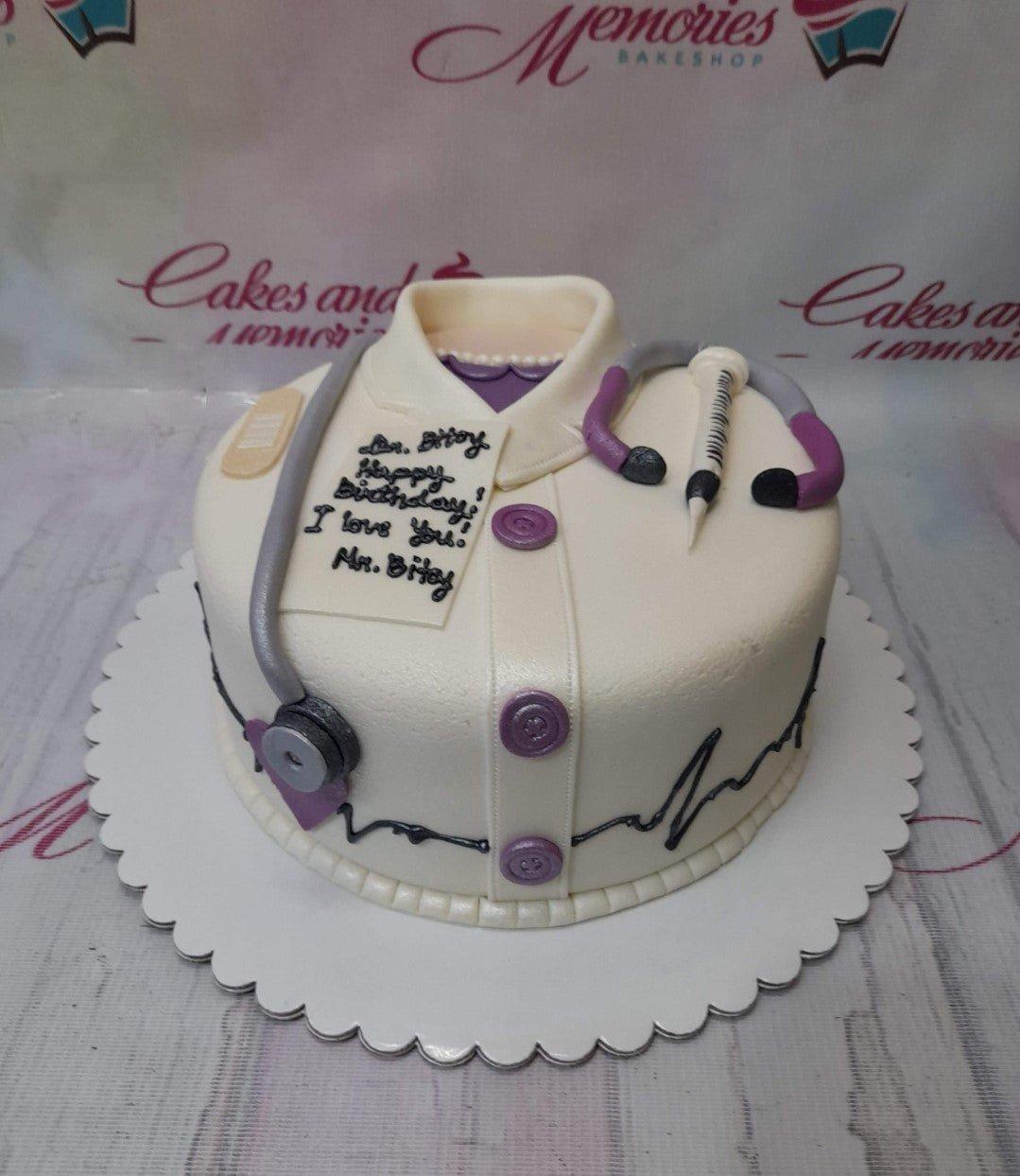 White fondant doctor-themed cake with a stethoscope, syringe, and purple buttons, featuring a birthday message for Dr. Bitoy.