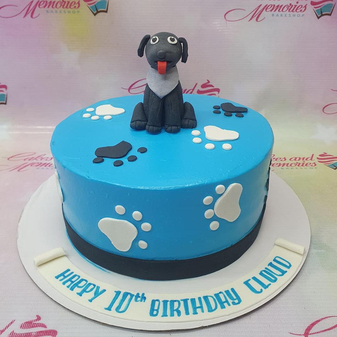 Blue dog themed birthday cake with a 3D black labrador fondant figure and white and black paw print decorations.