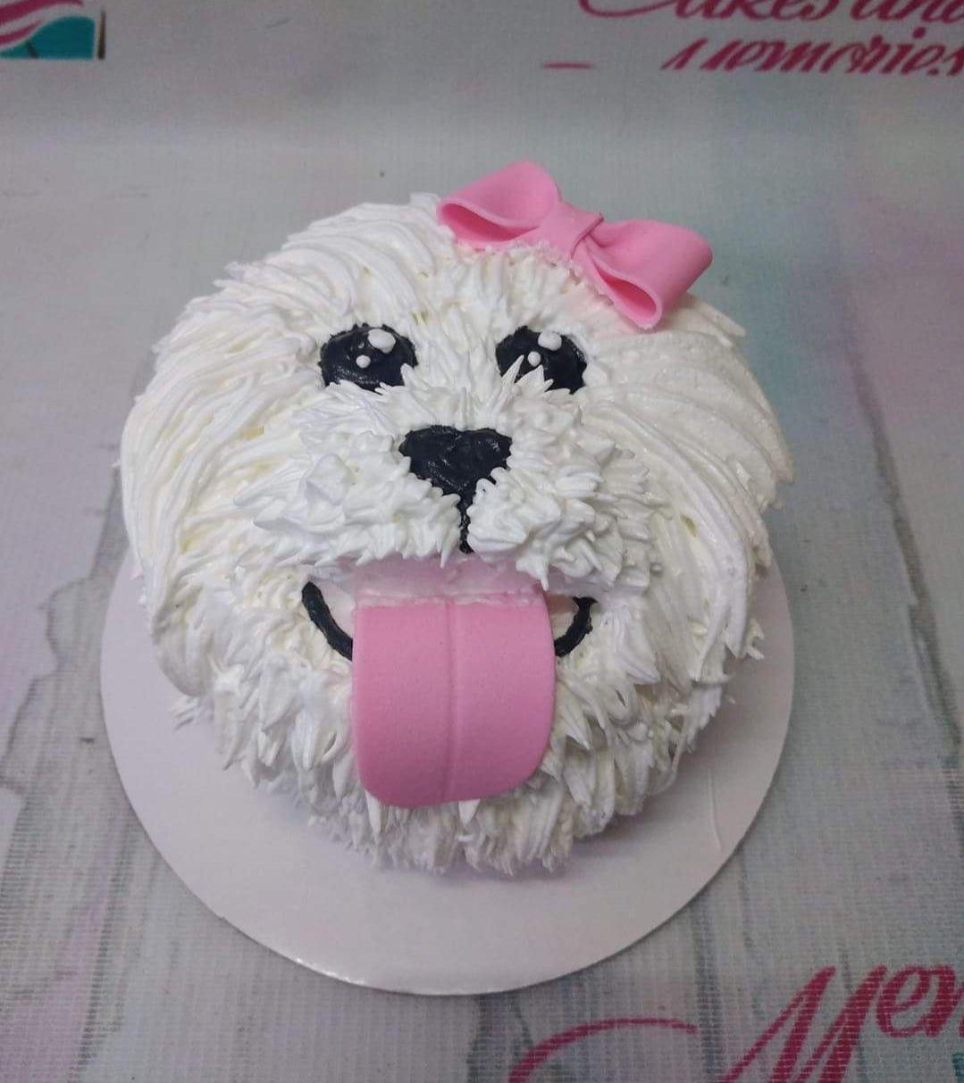 White dog-shaped cake with textured icing fur, pink fondant bow, and pink fondant tongue.