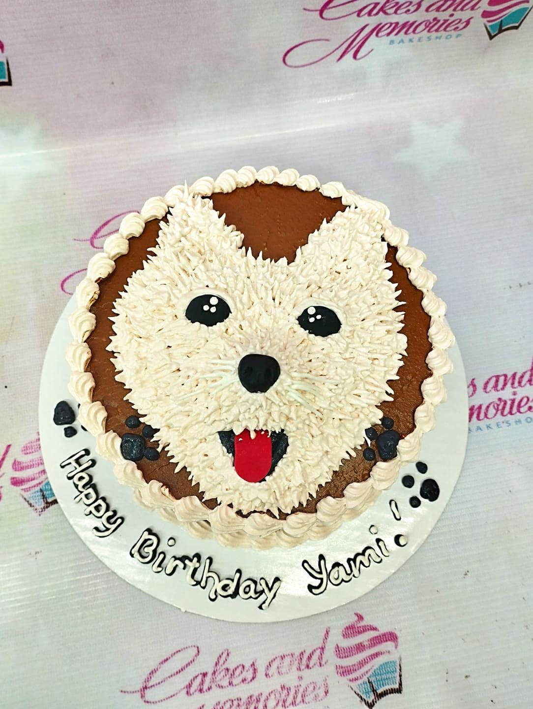 Round chocolate birthday cake with a white fluffy dog face design made of icing rosettes and black paw prints on the base board.