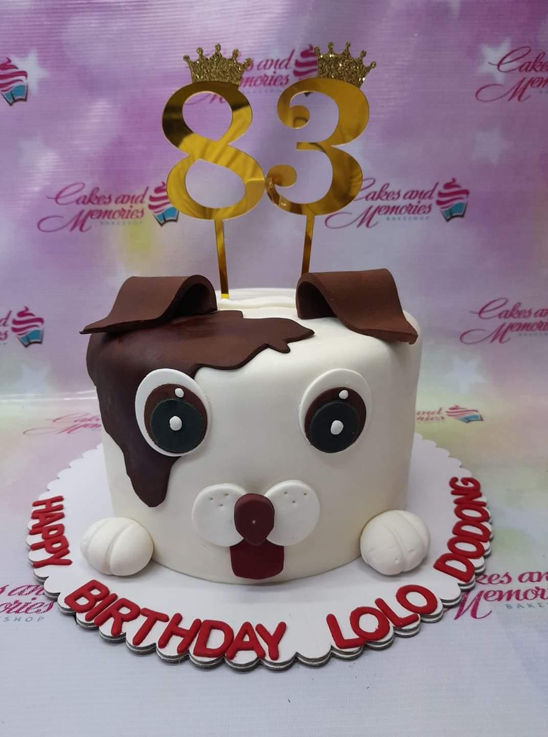 White fondant dog face cake with brown patches, floppy ears, and gold number 83 toppers for a birthday celebration.