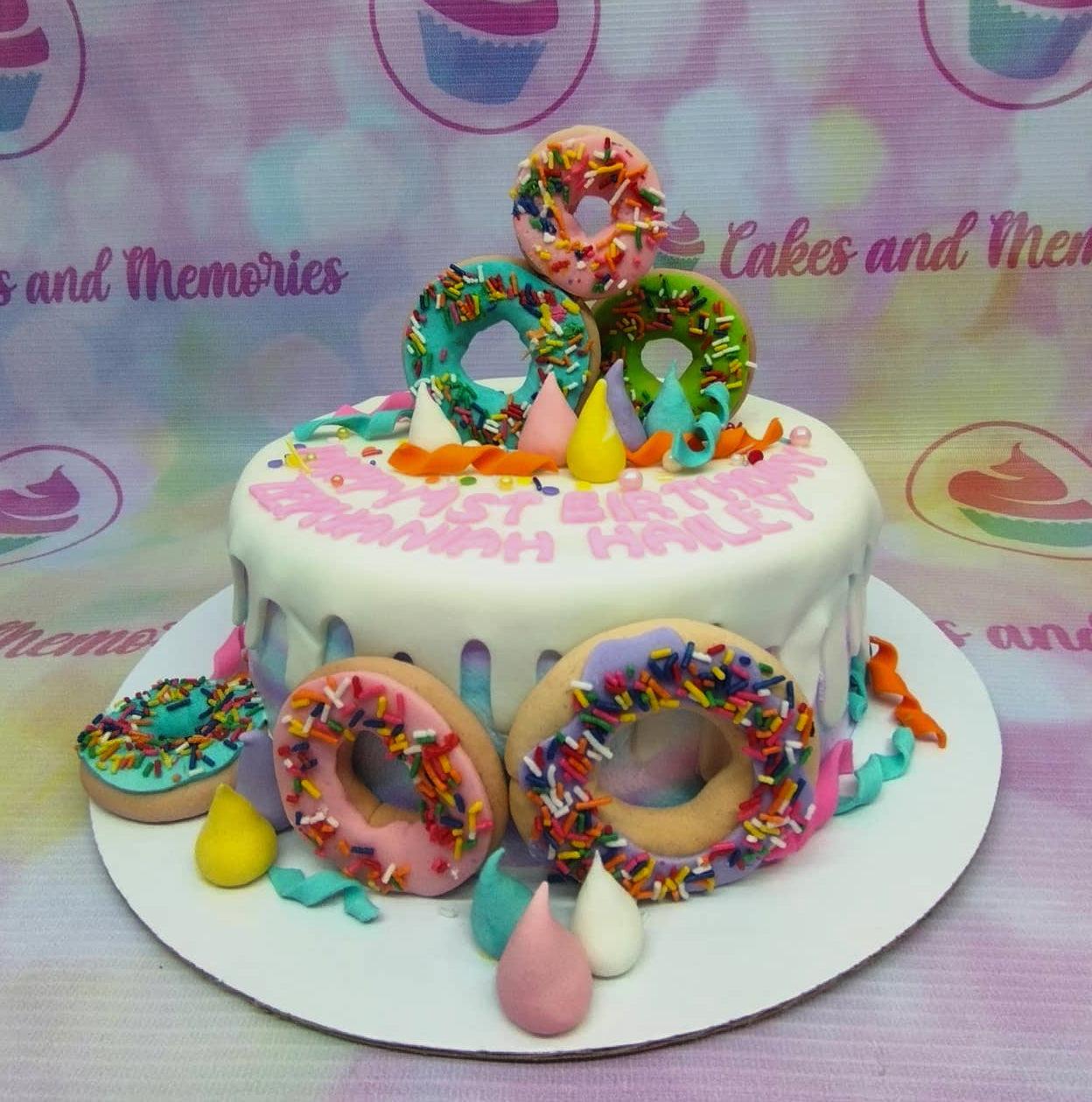 White drip cake decorated with colorful fondant donuts, sprinkles, and meringue kisses for a birthday celebration.