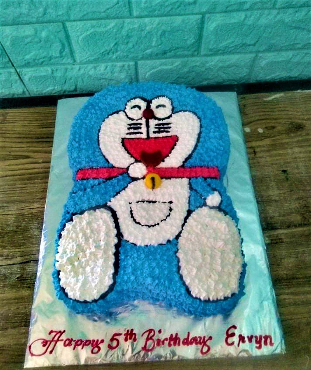 Doraemon character shaped cake with blue and white icing rosettes and a red collar detail.