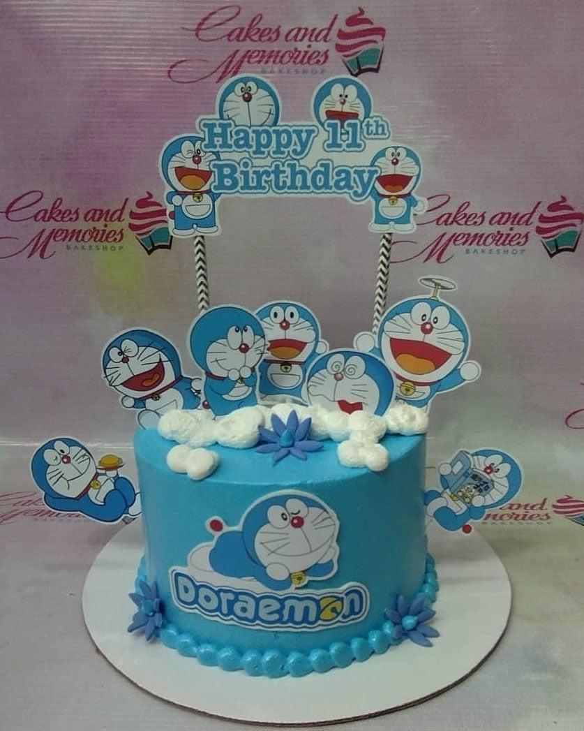 Light blue Doraemon themed birthday cake with multiple character printouts and white icing clouds.