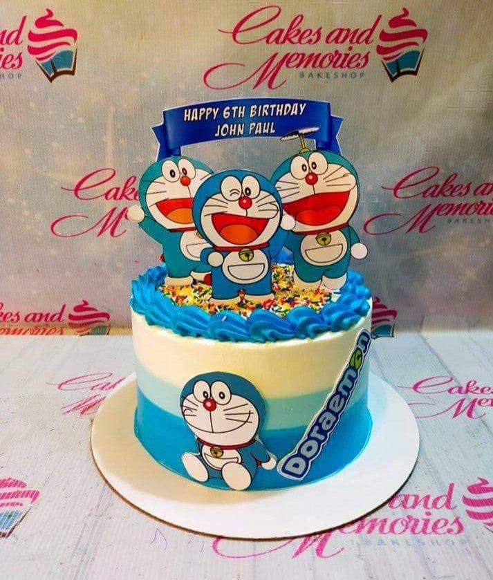 Doraemon themed birthday cake with blue and white gradient icing, character printouts, and colorful sprinkles.