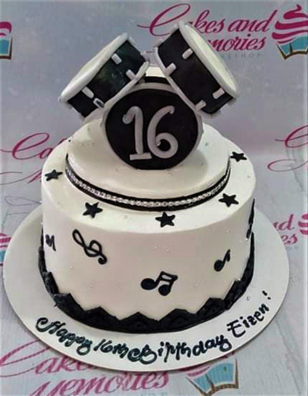 White 2-tier drum themed birthday cake with black musical notes, stars, and a 3D drum set topper for a 16th birthday.