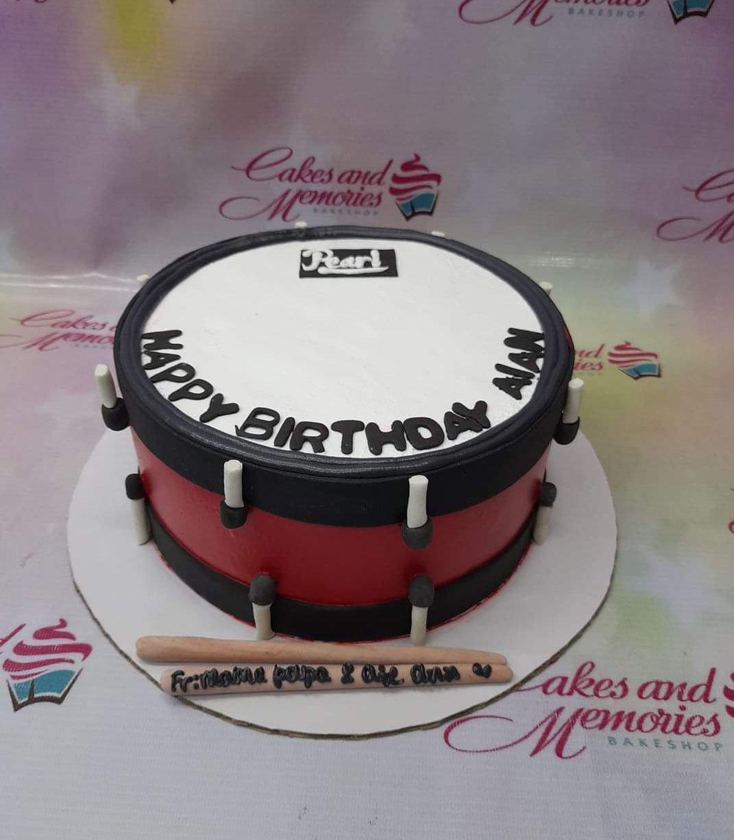 Red and black drum-shaped birthday cake with white top and drumstick decorations