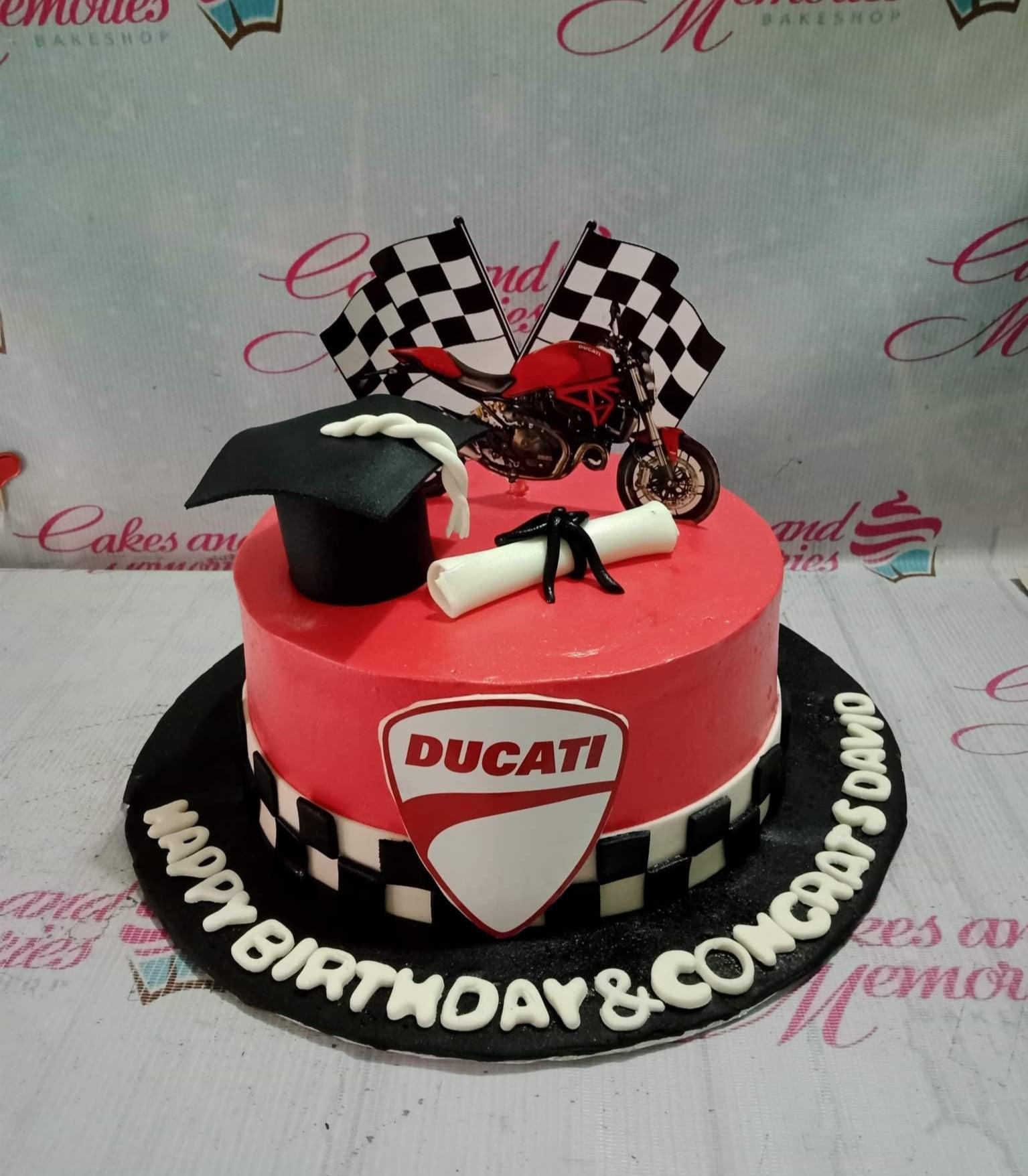 Red Ducati motorcycle and graduation themed cake with checkered flags, a graduation cap, and a diploma on a black base board.