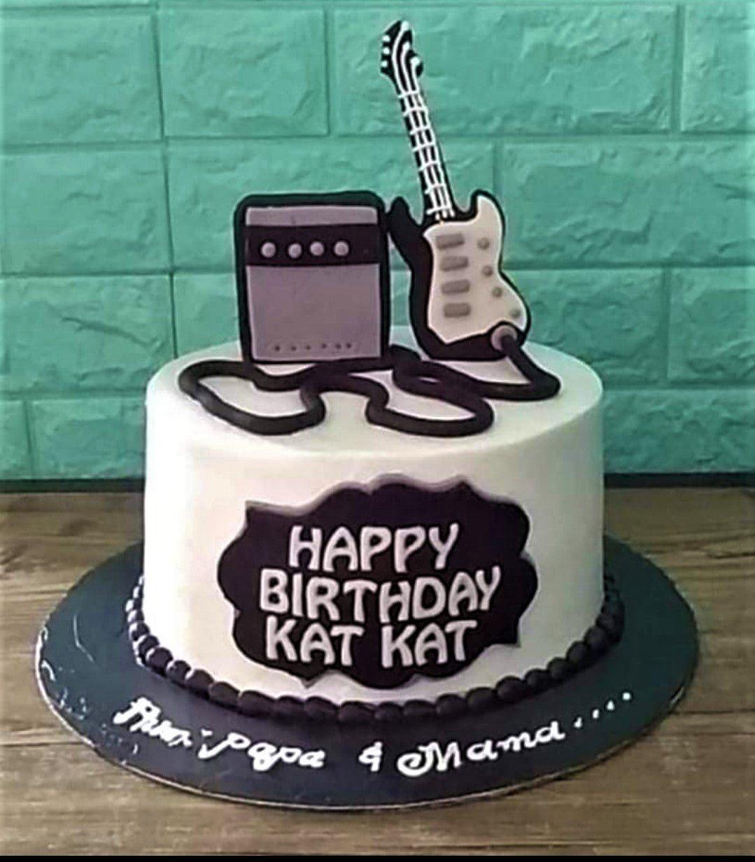 White minimalist birthday cake with a black electric guitar and amplifier topper, featuring a black plaque with white text.