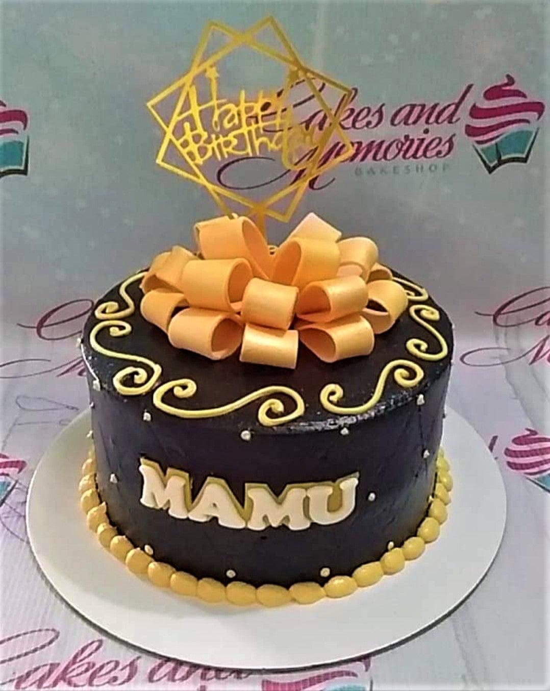 Black soft-icing cake with a large orange fondant bow, gold geometric Happy Birthday topper, and yellow icing swirls.