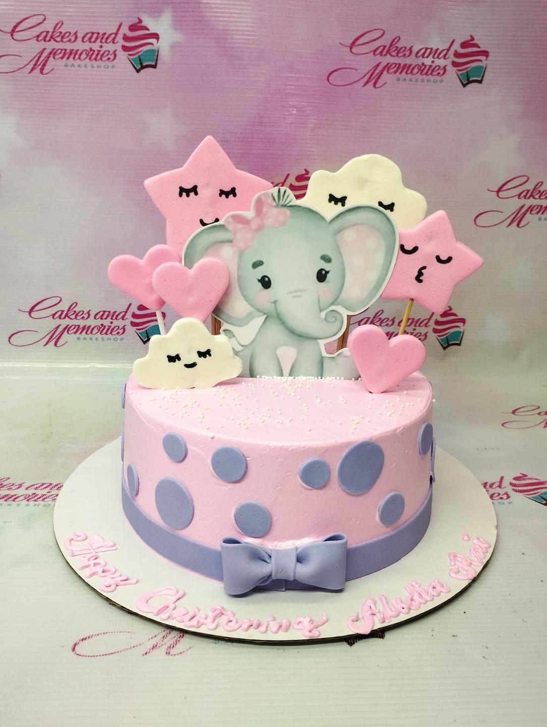 Pink elephant themed christening cake with pink stars, clouds, and hearts, featuring a cute elephant printout and purple polka dots.