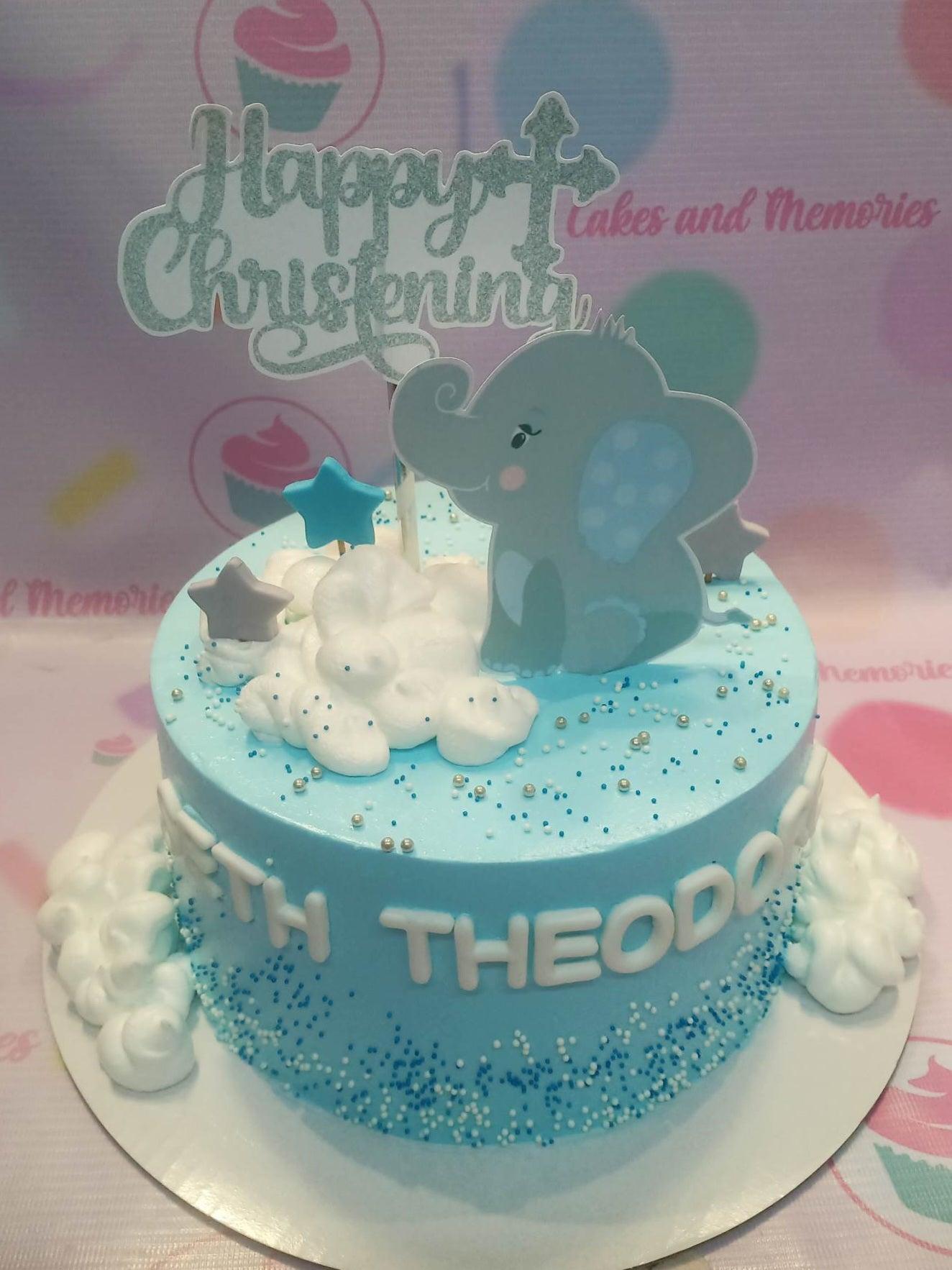 Light blue christening cake with a grey elephant printout topper, white icing clouds, and silver dragees.