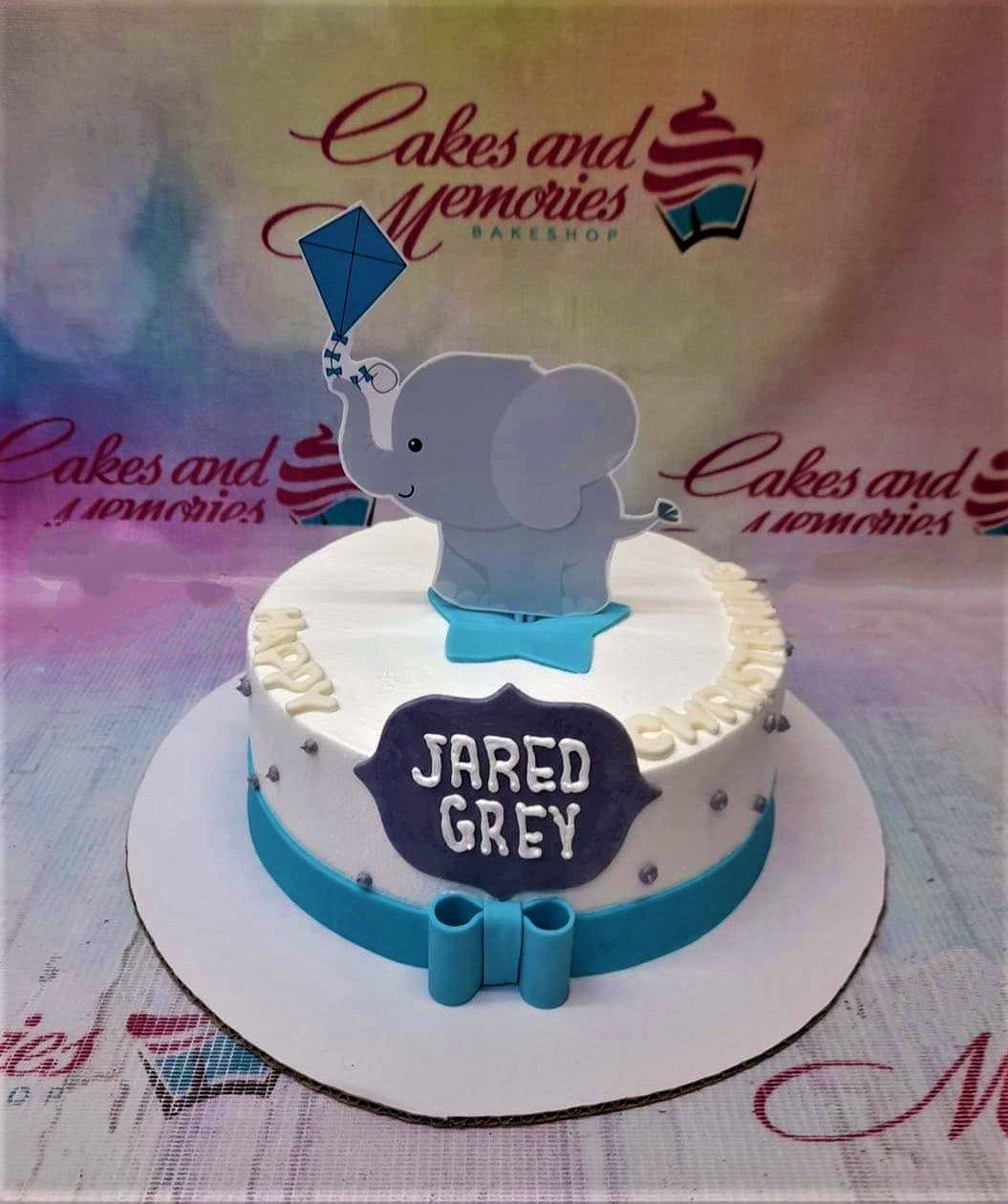 White 1-tier elephant christening cake with blue kite printout, blue ribbon base, and silver dragees.