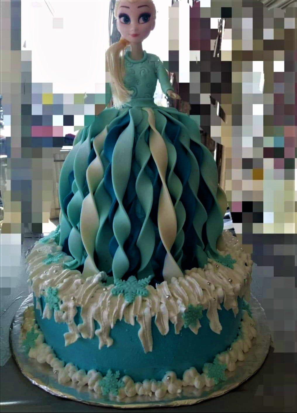 Elsa Frozen doll cake with a blue and white ruffled icing dress and snowflake decorations.
