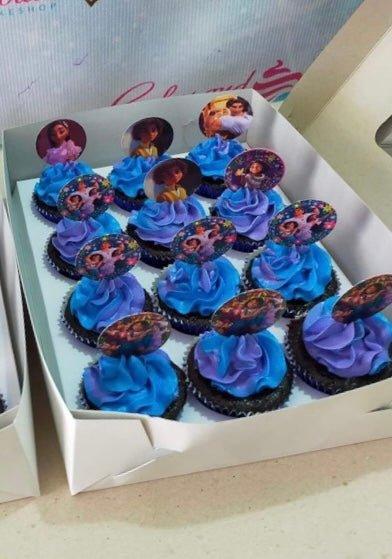A box of twelve chocolate cupcakes with blue and purple swirl icing topped with Encanto character printouts.