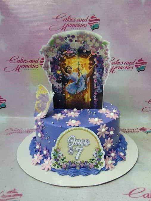 Purple Encanto themed birthday cake with Isabela printout topper, pink icing flowers, and silver dragees.