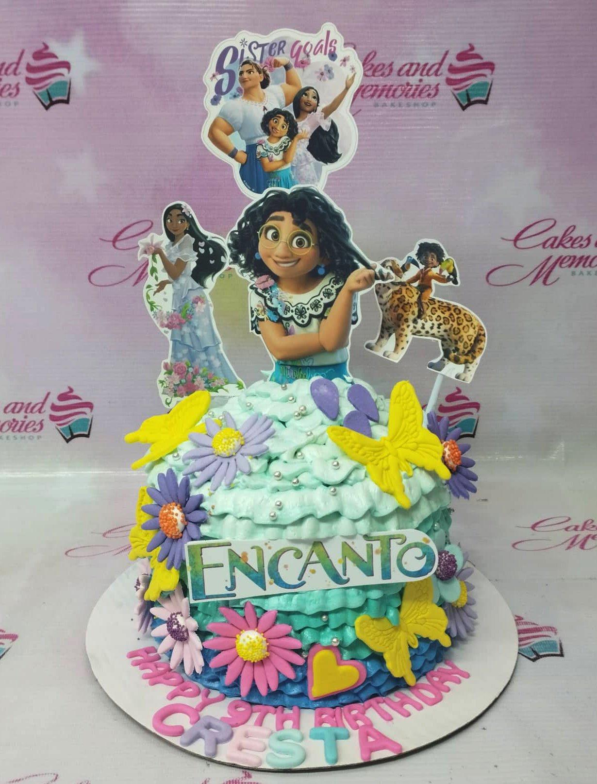 Encanto themed birthday cake with Mirabel, Isabela, and Antonio printouts, colorful icing ruffles, and fondant flowers and butterflies.