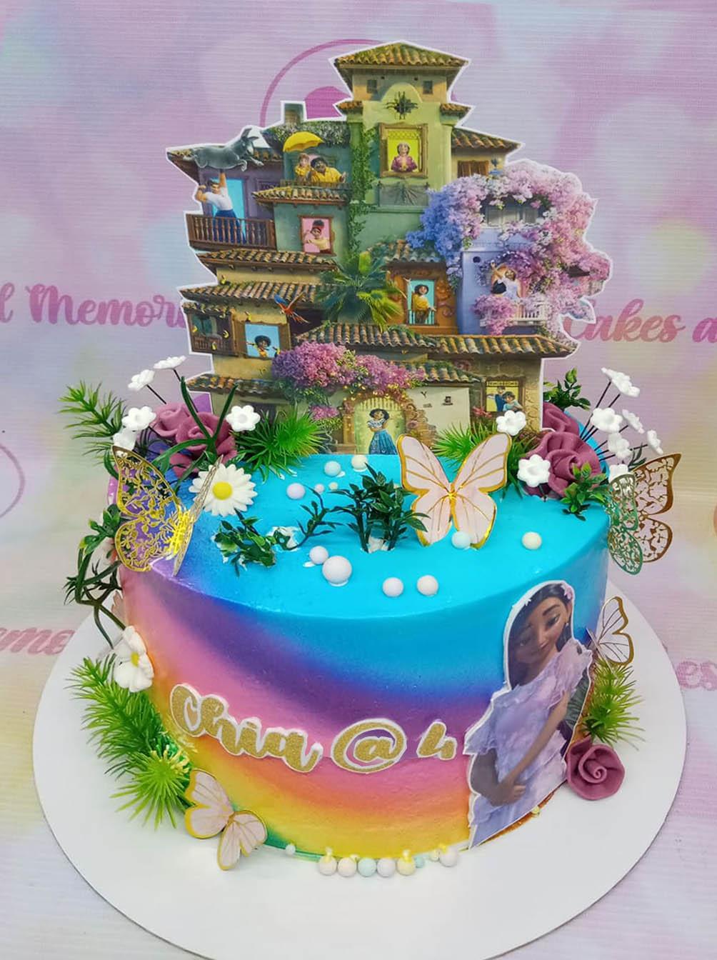 Encanto themed birthday cake with a colorful rainbow gradient icing, featuring the Madrigal house and Mirabel character printouts.
