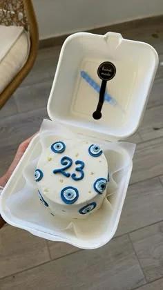 White bento cake with blue evil eye icing decorations and the number 23 in blue icing on top.