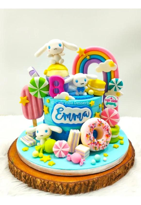 Vibrant blue Cinnamoroll themed birthday cake for Emma featuring a rainbow, donut, and various candy fondant decorations.