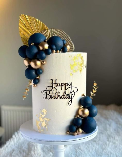 Elegant white 1-tier birthday cake with navy blue and gold spheres, gold leaf accents, and a black Happy Birthday topper.