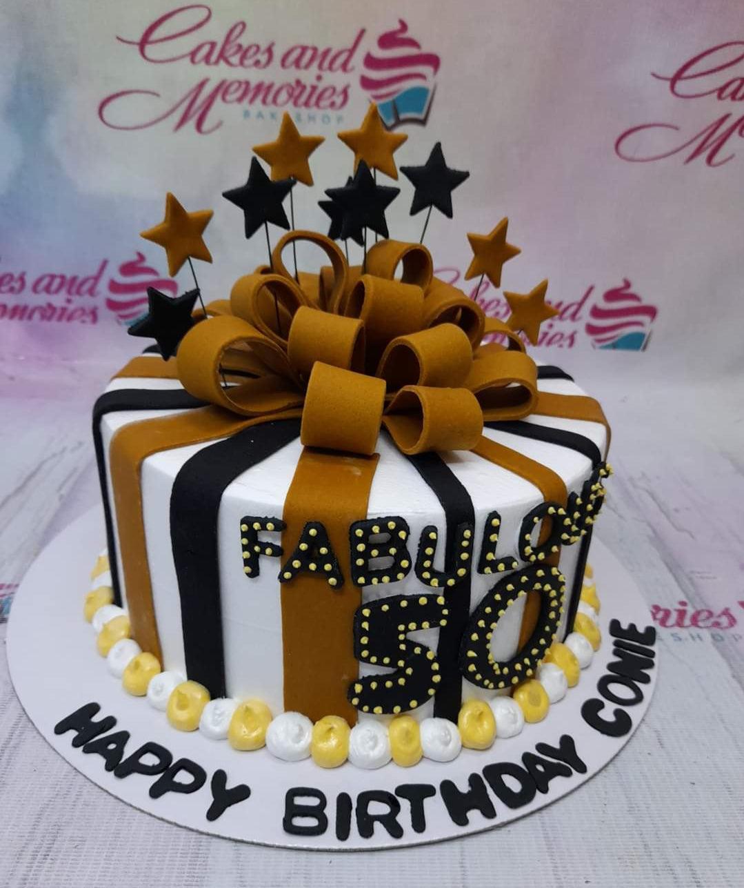 Black and gold striped birthday cake with a large fondant bow and star toppers for a 50th birthday celebration.