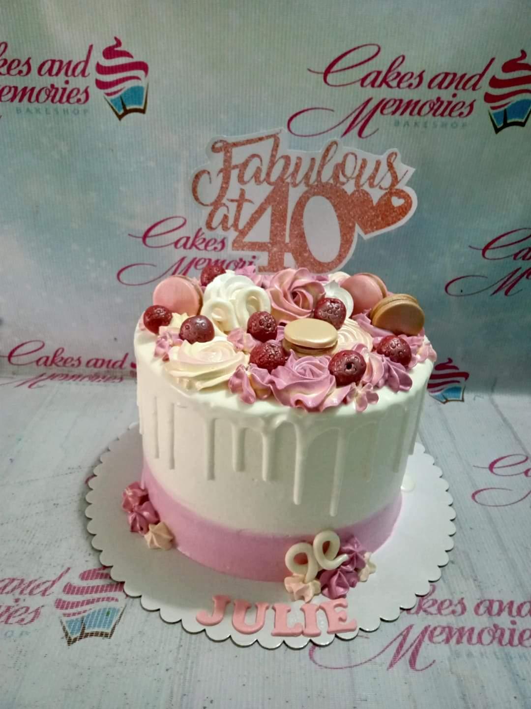 White and pink 40th birthday cake with pink icing rosettes, macarons, and a rose gold glitter Fabulous at 40 topper.