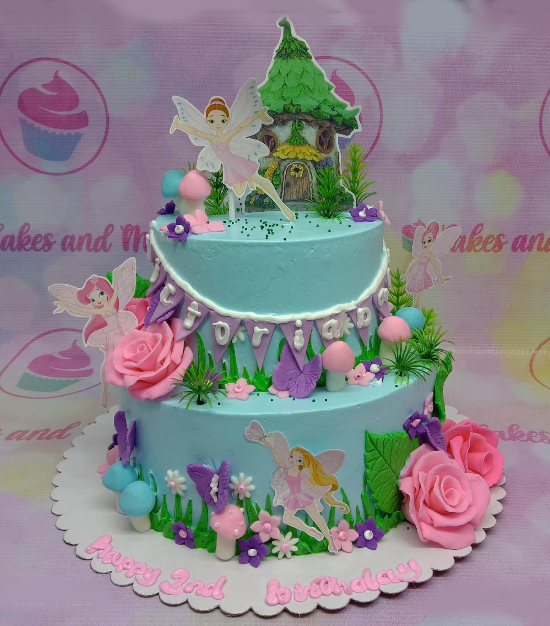Two-tier light blue fairy garden birthday cake with pink roses, mushrooms, and fairy printouts.