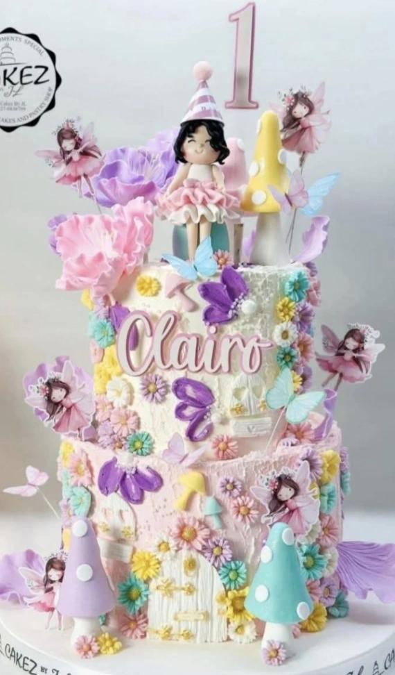 Two-tier fairy garden birthday cake with a girl figurine, mushrooms, butterflies, and colorful icing flowers in pink, purple, and teal.