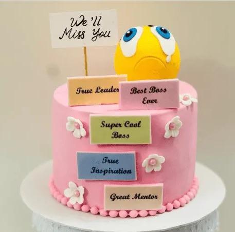 Pink cake with a yellow sad face emoji topper and plaques saying Best Boss Ever and True Leader
