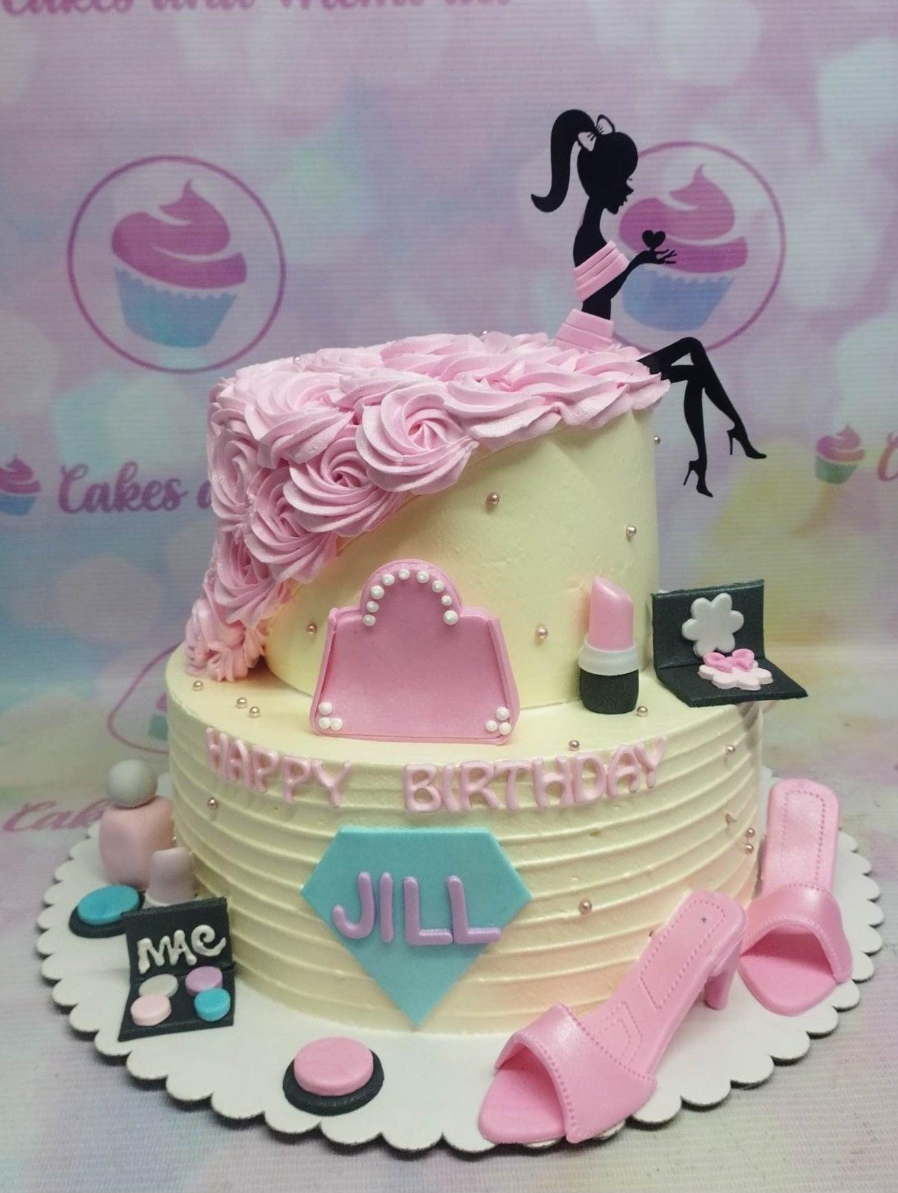 Two-tier pink and cream fashion-themed birthday cake with a silhouette topper, fondant makeup items, and pink icing rosettes.