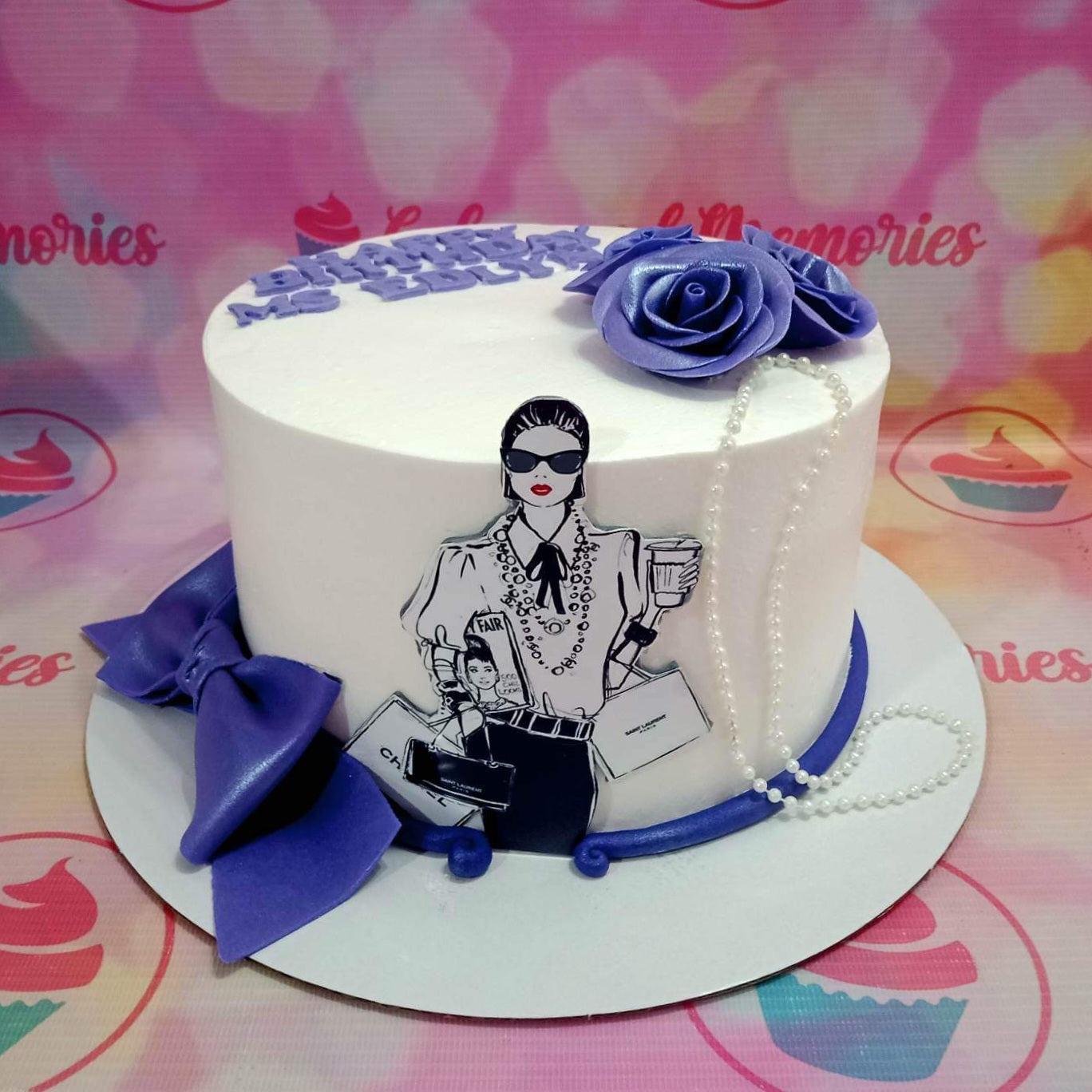 White minimalist cake with purple fondant roses, a fashionista printout topper, pearl necklace, and a large purple bow on the base.