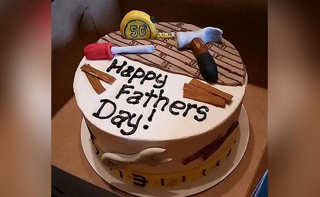 White round cake for Father's Day featuring edible fondant tools like a hammer, screwdriver, tape measure, and wood planks.