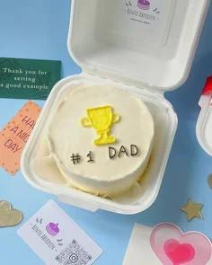 White bento cake with a yellow piped icing trophy and black icing text reading #1 DAD in a white box.