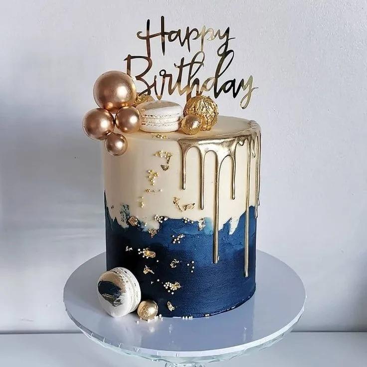 Elegant navy blue and white 1-tier cake with gold drip, gold spheres, macarons, and a gold Happy Birthday topper.