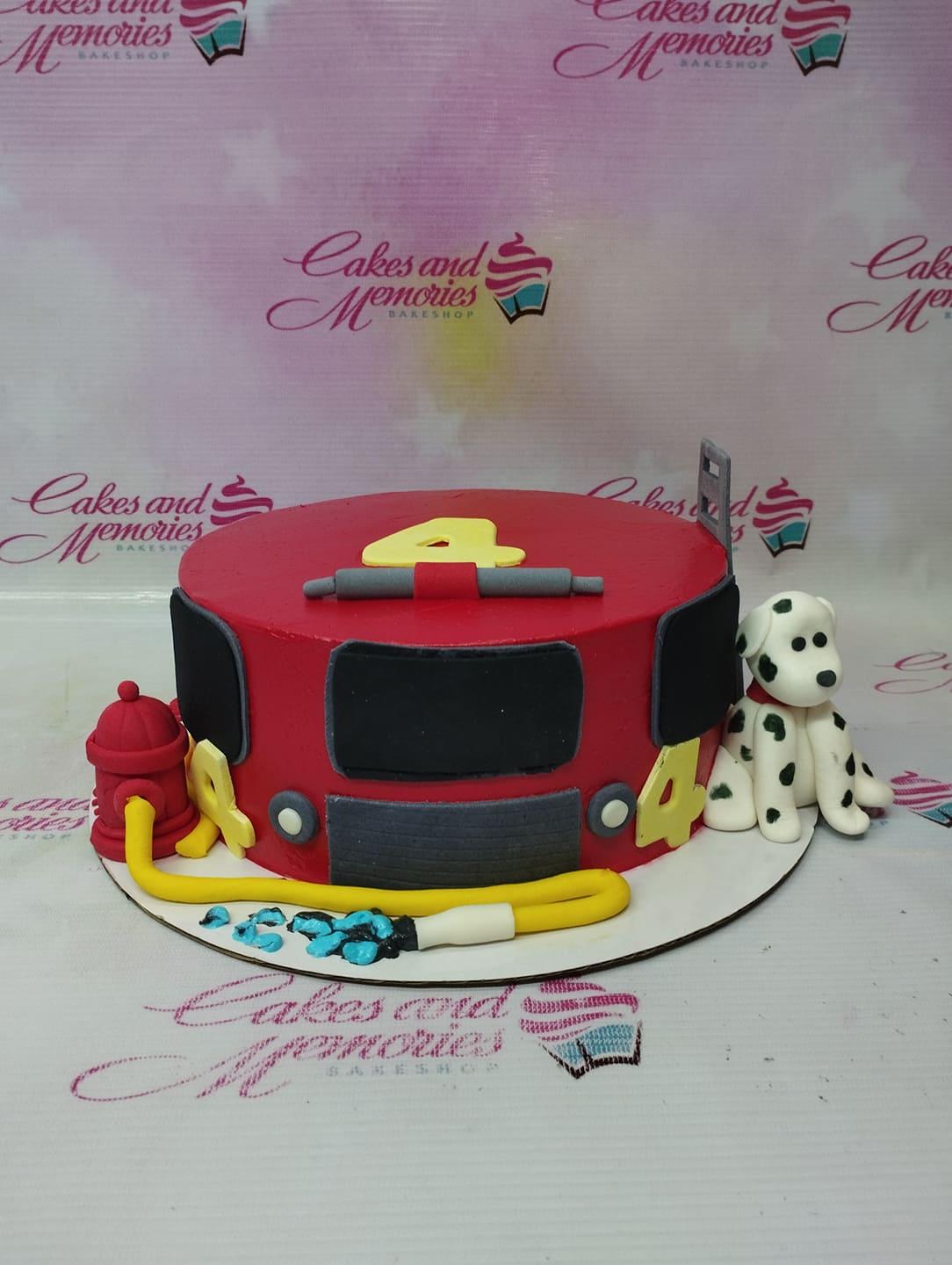 Red fire truck themed birthday cake with a fondant dalmatian dog, fire hydrant, and yellow hose.