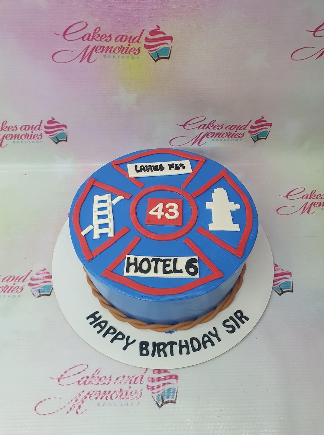 Blue firefighter themed birthday cake with red Maltese cross design and white ladder and hydrant fondant accents.